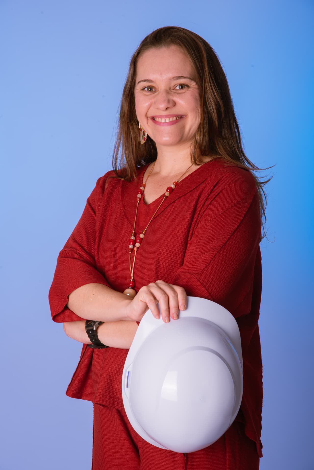 Lucila Fiorelli sorrindo, com roupa vermelha e segurando um capacete branco diante de um fundo azul
